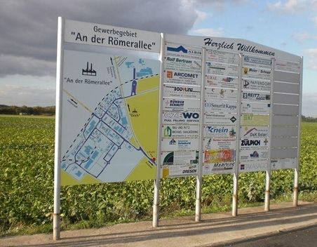 Verschiedene Infotafeln und Wegweiser an einem Feld