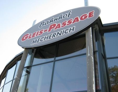Schild der Bahnhofs Gleis-Passage Mechernich an einem modernen Glasgebäude