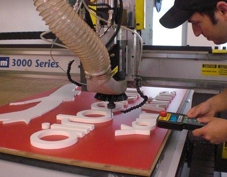 CNC-Maschine, die weiße Buchstaben auf eine rote Tafel schneidet